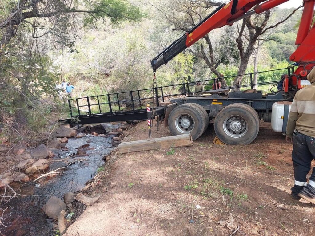 Crane truck placing a steel footbridge across a river